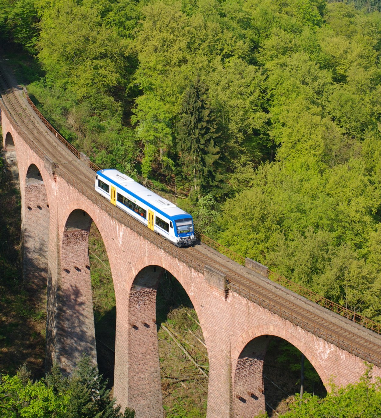 Das Hubertus-Viadukt (Hubertusschluchtbrücke) führt in einer Kurve über die Hubertusschlucht. Das Bauwerk hat sechs Öffnungen auf einer Länge von 150 m bei einer Höhe von 50 m. Zum Zeitpunkt der Errichtung 1908 war es die höchste Steinbogenbrücke Deutschlands.
Die Brücke wurde aus bossierten Rotsandsteinquadern aus der Neckargegend errichtet. Die Unterseiten der Bögen sind mit Backstein verblendet. Aus den Pfeilern ragen auf Höhe des Kämpfers Eisenträger für das Lehrgerüst hervor. Der abschließende getreppte Konsolenfries auf beiden Seiten der Brücke trägt durch Eisengitter gesicherte Seitenwege. Jeder zweite Brückenpfeiler ist durch ein getreppt ausgekragtes steinernes Brüstungsstück abgeschlossen. | © Transdev SE & Co. KG