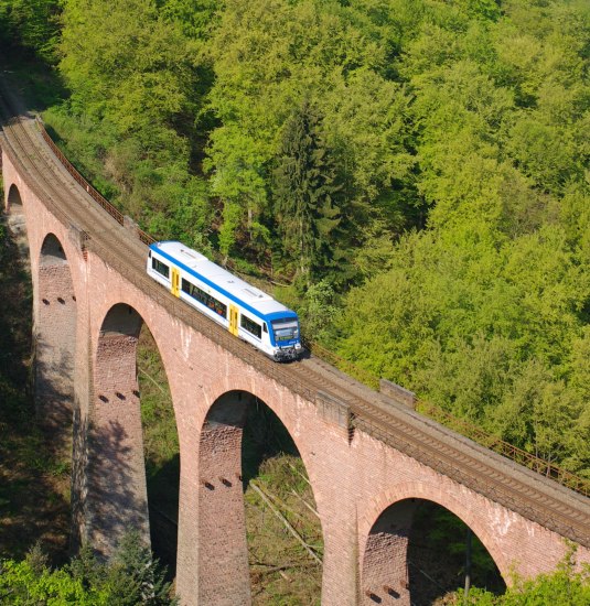 Das Hubertus-Viadukt (Hubertusschluchtbrücke) führt in einer Kurve über die Hubertusschlucht. Das Bauwerk hat sechs Öffnungen auf einer Länge von 150 m bei einer Höhe von 50 m. Zum Zeitpunkt der Errichtung 1908 war es die höchste Steinbogenbrücke Deutschlands.
Die Brücke wurde aus bossierten Rotsandsteinquadern aus der Neckargegend errichtet. Die Unterseiten der Bögen sind mit Backstein verblendet. Aus den Pfeilern ragen auf Höhe des Kämpfers Eisenträger für das Lehrgerüst hervor. Der abschließende getreppte Konsolenfries auf beiden Seiten der Brücke trägt durch Eisengitter gesicherte Seitenwege. Jeder zweite Brückenpfeiler ist durch ein getreppt ausgekragtes steinernes Brüstungsstück abgeschlossen. | © Transdev SE & Co. KG